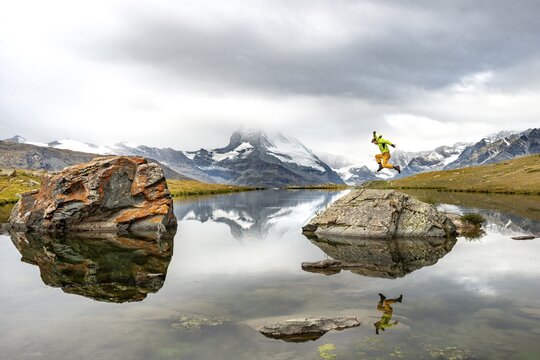 Hiker jumps on rocks in the lake, Lake Stellisee, Matterhorn, cloudy, Wallis, Switzerland