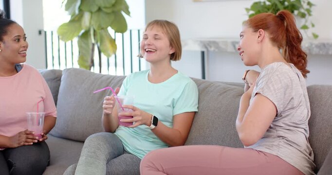 Diverse female friends welcoming newcomer entering, sipping pink drinks and catching up on sofa
