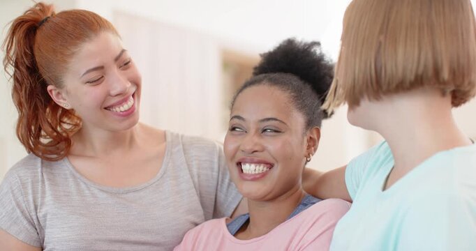 Three women on couch, center woman in pink smiling, encouraging friends holding forearms in support