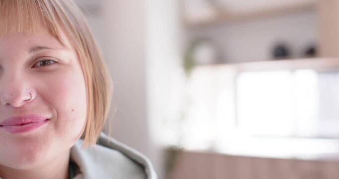 Woman responding to prompt, smiling then laughing by bright window in light hoodie, copy space
