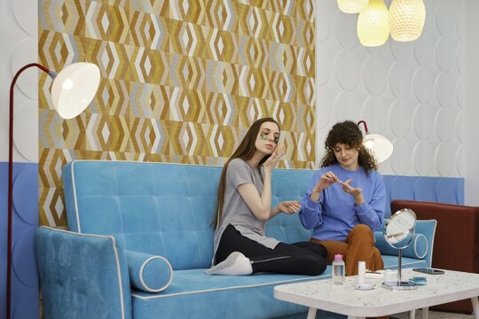 Girlfriends sit at home on the couch and take care of the skin of the face. One applied patches under the eyes, and the other squeezed the serum on the finger