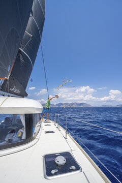 Young man throws food scraps overboard, sailing on a catamaran, Dodecanese, Greece