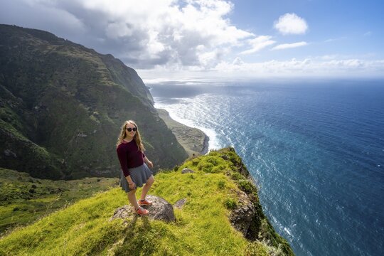 Young woman enjoying view of cliffs and sea, coastal landscape, viewpoint Ponta da Leideira, near Calhau das Achadas, Madeira, Portugal