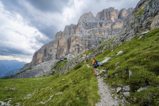 Female mountaineer on a hiking trail in front of Rifugio Maria E Alberto Ai Brentai, mountainous landscape with steep rock faces, Brenta-Adamello Natural Park, Trentino, Italy