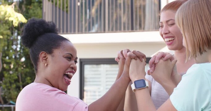 Three female friends linking hands greeting letting go hugging showing square smartwatch on patio