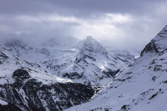 Dark clouds and wafts of mist surround the snow-covered summit of Mount Le Besso, view from the Sorebois summit station, Val d'Anniviers, Valais Alps, Canton Valais, Switzerland