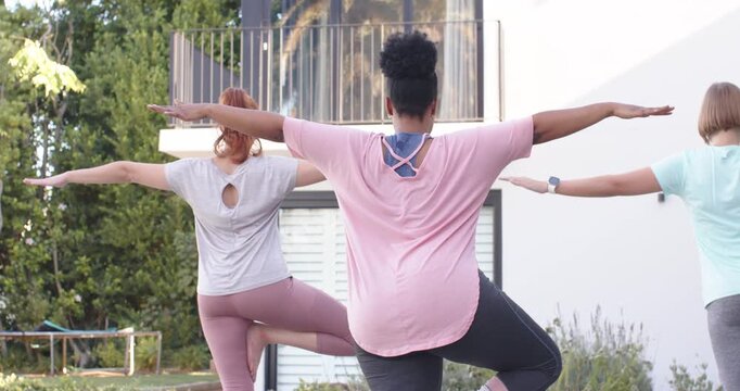Female friends following center woman shifting weight, practicing balance in yard with smartwatch