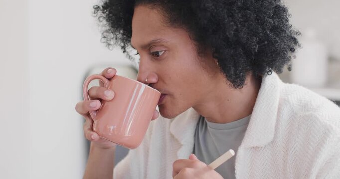African American man sniffing pink mug, holding stirrer, sipping while listening in home kitchen