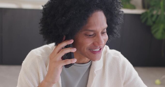 Man answering call, raising smartphone to right ear, laughing, preparing notes at table