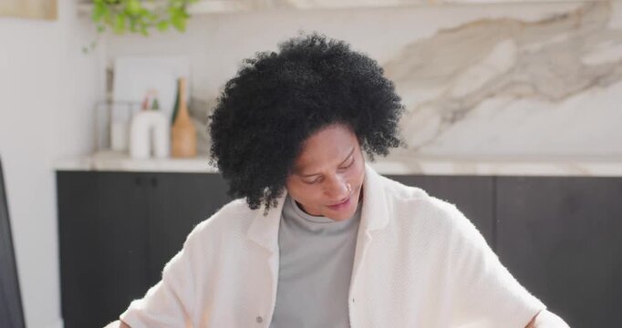 African American man checking tablet, annotating papers with pen, typing on laptop for work at home
