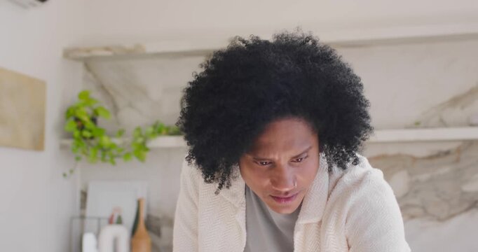 African man starting by leaning at kitchen table, tapping tablet and taking notes for work