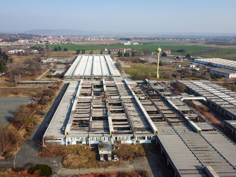 Aerial view of a large industrial complex with long flat roofs and a yellow water tower surrounded by fields and the town in Scarmagno, Piedmont, Italy.