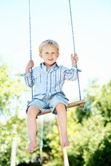 Obraz premium Child, portrait and play on swing at playground, fine motor skills and development in nature and fun. Outdoor, park and kid with smile on weekend, growth and boy with positive attitude or fresh air