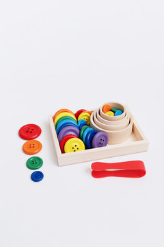 Colorful wooden buttons lined up next to a sorting tray and tweezers. High vertical headspace for clean typographic layouts and educational posts.