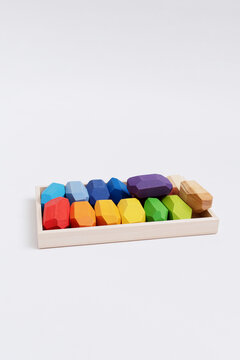 Colorful wooden balancing gems inside a tray on a white background. Vertically oriented composition with large empty headspace at the top for copy.