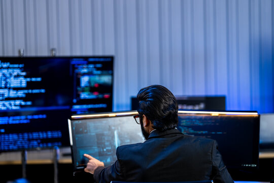South Asian male network security expert in a dark blazer explains endpoint protection in a blue-lit cybersecurity operations center with data screens behind him.