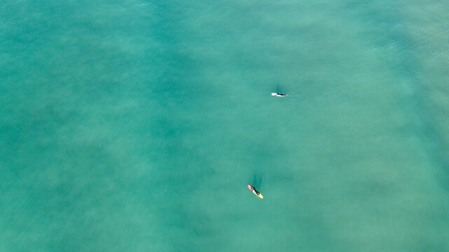 Aerial view of two surfers on their boards in the clear turquoise sea water off the coast of Perranporth, Cornwall, United Kingdom.