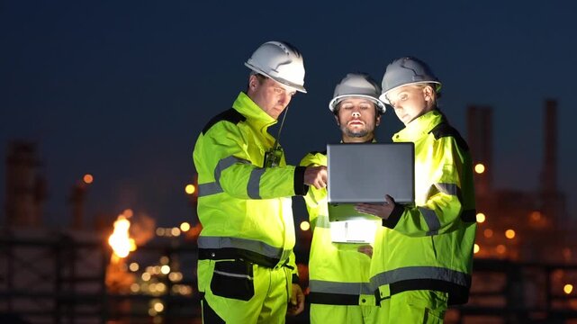 Engineer inspection at industrial refinery, safety hardhat, high visibility jacket, laptop night shift team reviewing maintenance data, site audit planning repairs under flare stack and plant lights