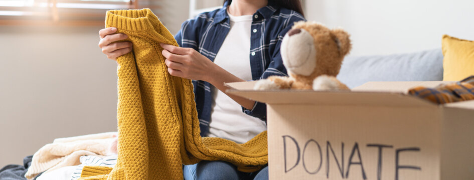 Close up of young Asian woman packing clothes and teddy bear into donation box at home