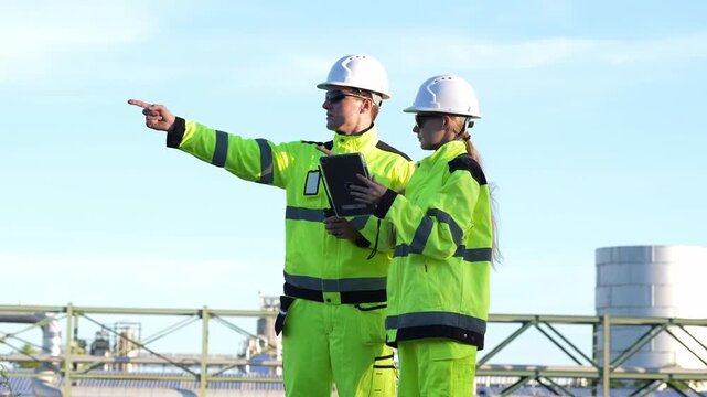 Engineering inspection industrial engineer safety hard hat high visibility clipboard coordinate maintenance, review site plan, point toward equipment at factory plant under clear sky