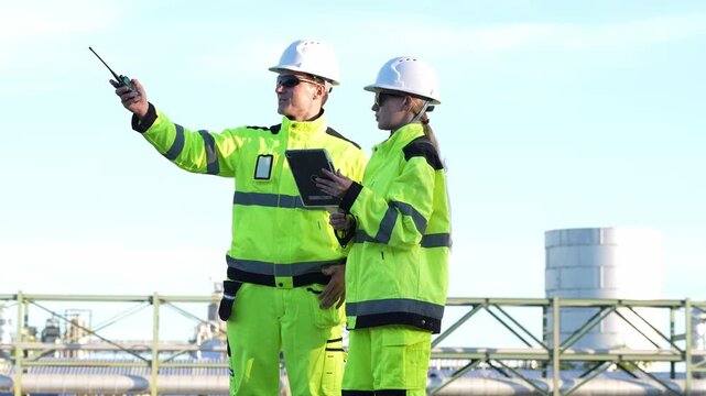 Engineering inspection industrial safety engineer hard hat high visibility communication via radio and tablet at refinery platform site, team coordinating maintenance planning, audit risk control