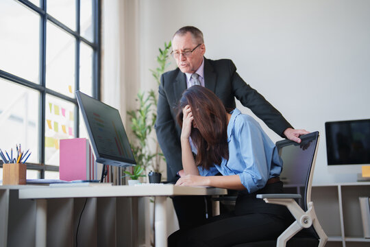 Stressed businesswoman covering her face at an office desk while an angry male boss stands over her, creating a tense work environment and professional conflict