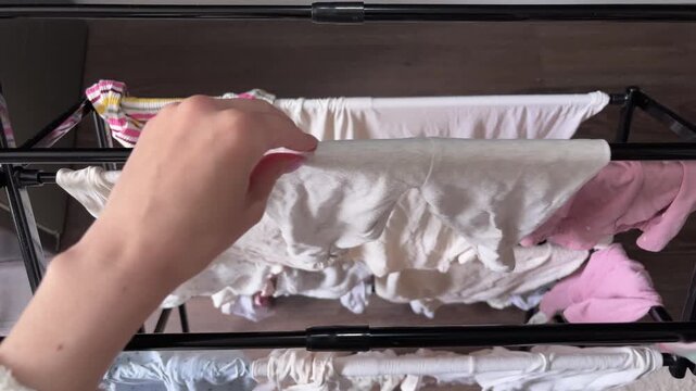 A woman's hands are taking clean children's laundry off the drying rack
