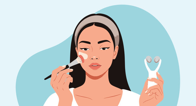 Beautiful woman applying liquid foundation with a makeup brush while holding a facial massage tool in her other hand.