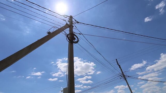 Low angle view of utility poles and overhead power lines crossing sunny blue sky