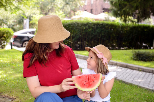 Mother and daughter sharing a watermelon in a sunny park. Warm family bonding, healthy summer snack, childhood happiness, outdoor lifestyle, and loving parenthood concept