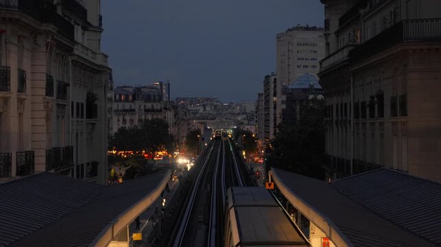A passenger metro train departs an elevated station and moves along urban tracks at dusk in Paris France. Metropolitan public transport transit infrastructure, city commuter evening voyage.