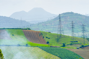Scenic view of agricultural terraced fields on the slopes of a mountain in indonesia with high voltage transmission towers under a hazy sky © RifaldiMuhammadSalim