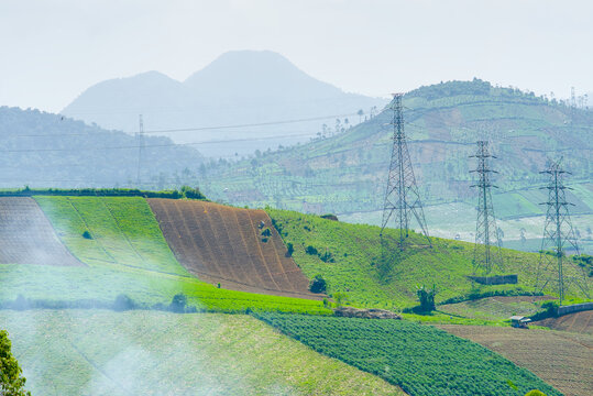 Scenic view of agricultural terraced fields on the slopes of a mountain in indonesia with high voltage transmission towers under a hazy sky