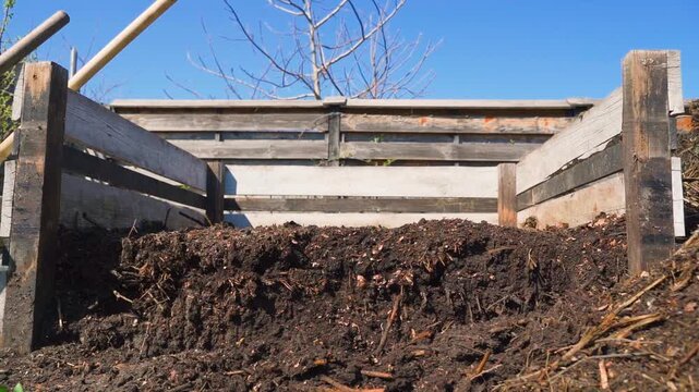 Wooden compost bin with decomposed dark soil in garden
