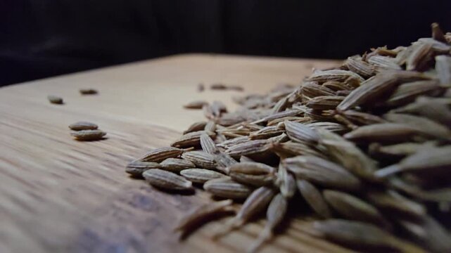 Macro close-up shot of dry cumin seeds scattered on a wooden surface, highlighting their texture and organic details.