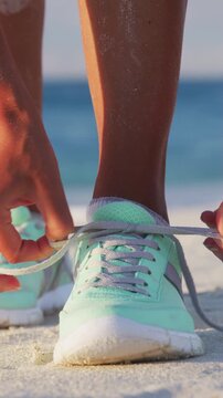 Vertical video of runner woman tying laces of running shoes preparing for beach jogging. Closeup of hands lacing sneakers trainers for cardio workout. Female athlete living a fit and active life.