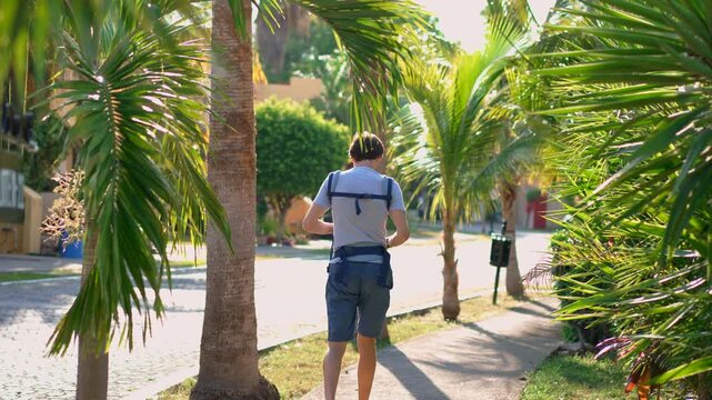 Father carrying infant son through sunny tropical sidewalk. Slow motion.