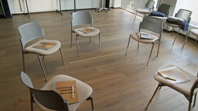 Empty chairs arranged in circle holding psychology therapy support group folders. Clip representing concept for mental health awareness campaigns or community counseling advertisements