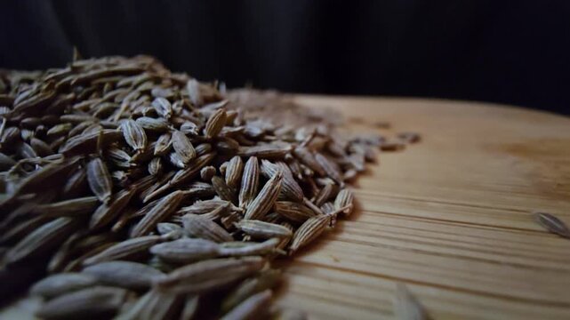 Close-up macro shot of organic raw cumin seeds scattered on a wooden surface, highlighting the textured details of the spice, perfect for culinary and healthy eating content.