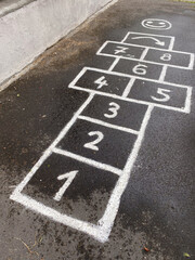 Fototapeta premium Traditional hopscotch game drawn with white chalk on wet dark asphalt.