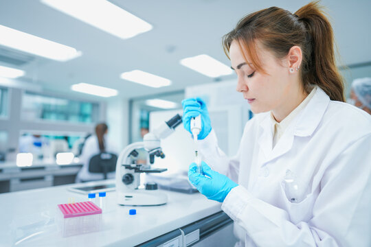 Pharmaceutical researcher performing precise chemical aliquot application on test slide. Young scientist validating biochemical compound reaction in modern biotech lab.