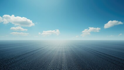 Obraz premium Large empty asphalt ground framed by a clear sky with gentle white clouds