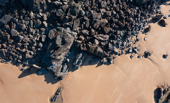 Aerial view of the dark jagged rocks of Bedruthan Steps meeting the golden sand on the beach in Padstow, Cornwall, United Kingdom.