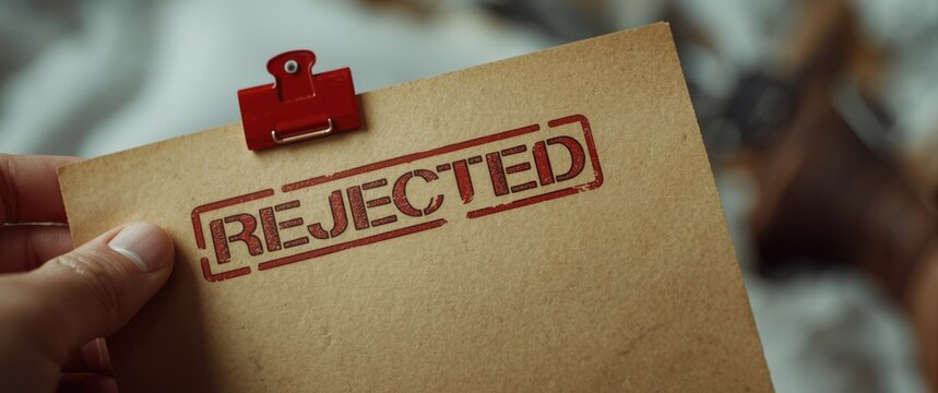 Hand holding a rejected application letter with a red stamp