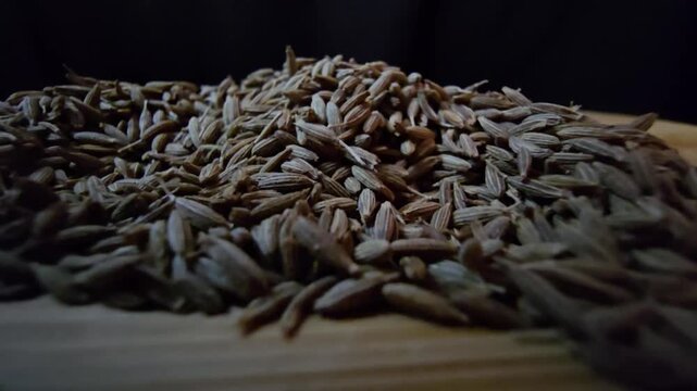 Macro close-up shot of dry cumin seeds scattered on a wooden surface, highlighting their texture and organic details.