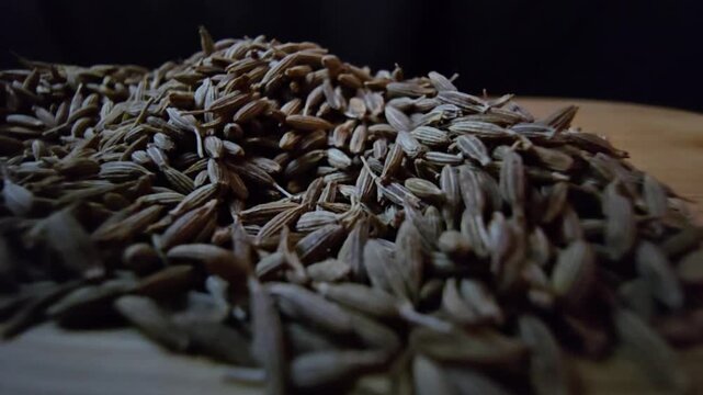 Macro close-up shot of dry cumin seeds scattered on a wooden surface, highlighting their texture and organic details.
