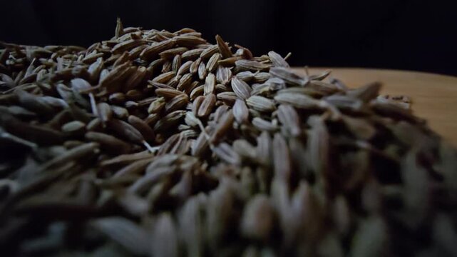 Macro close-up shot of dry cumin seeds scattered on a wooden surface, highlighting their texture and organic details.