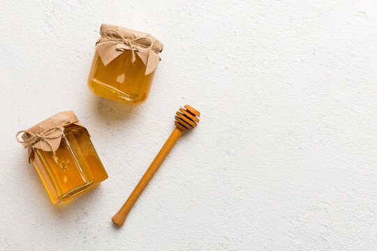 Glass jar of honey with wooden drizzler on colored background. Honey pot and dipper high above. Top view copy space