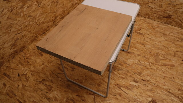 Wooden chipboard piece on a white folding table in a carpentry workshop. Particle board plate top view on oriented strand board wood texture background. Construction material and renovation concept