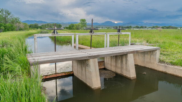 irrigation ditch with flowing water in northern Colorado, three headgates, lifting gear and foot bridge